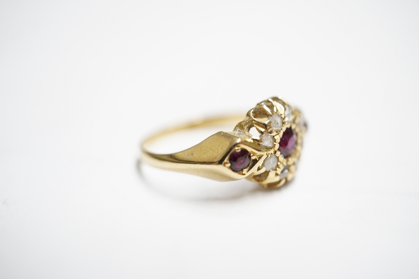 An early 20th century yellow metal and three stone ruby set ring, the centre stone bordered with rose cut diamonds, size H/I, gross weight 2.8 grams.